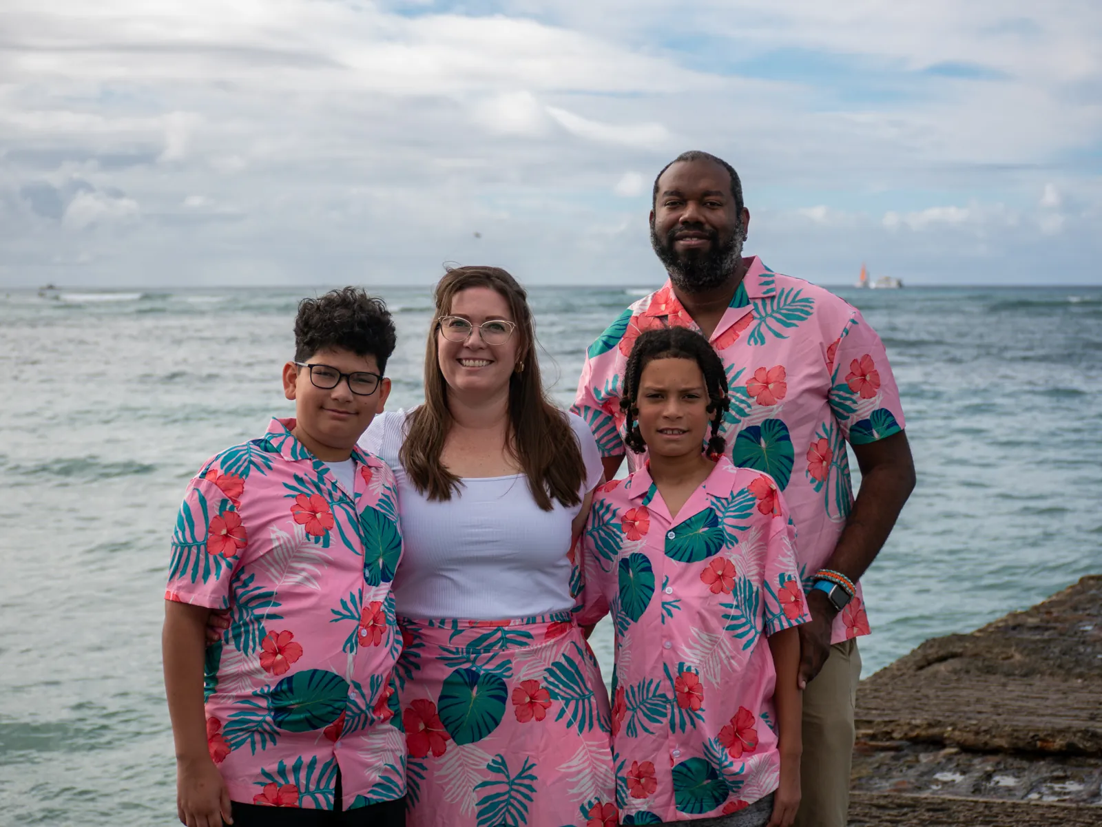 The FM Tech owner standing with his wife and two children, all in matching pink tropical-print shirts, on a rocky shoreline
