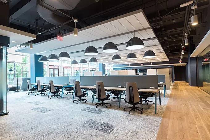 Open-plan commercial office with rows of desks, task chairs, and black pendant lights