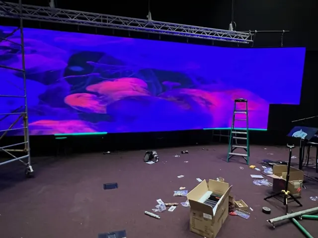 Large LED display above a church stage with a ladder and installation materials nearby