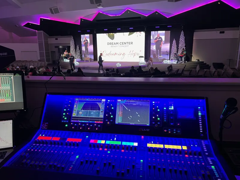 Audio mixing console in the foreground with a church stage and LED screens behind it