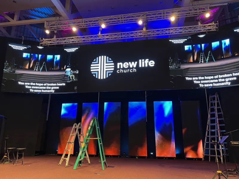 Church stage with a wide central LED screen, side displays, and ladders set up in front